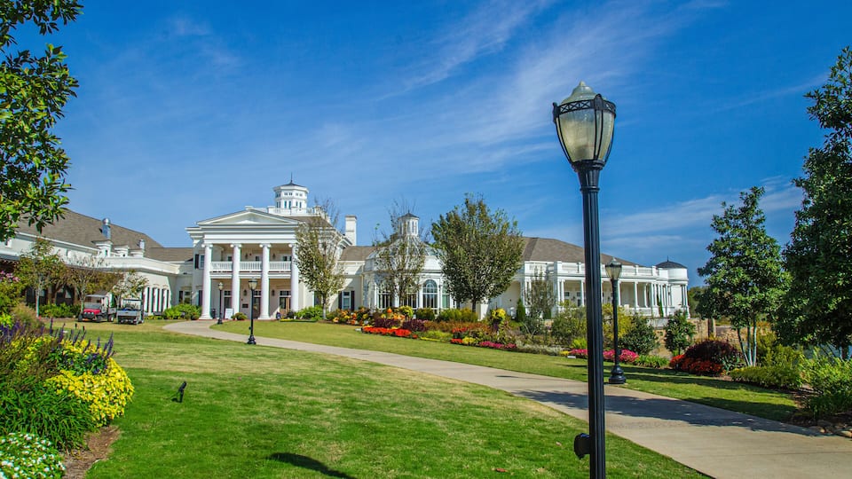 A large white building with columns and a dome, surrounded by well-maintained lawns and colorful flower beds.