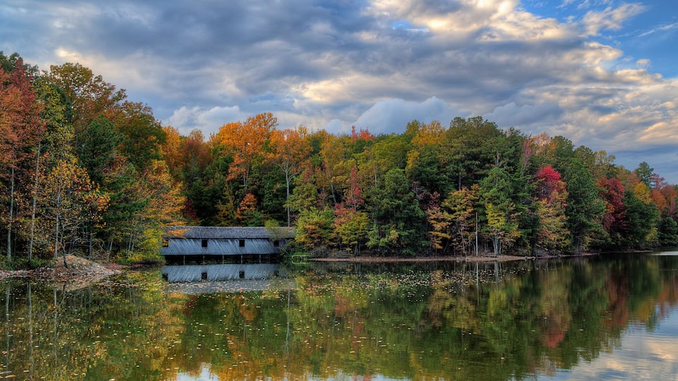 A serene lake with autumn-colored trees and a rustic cabin.