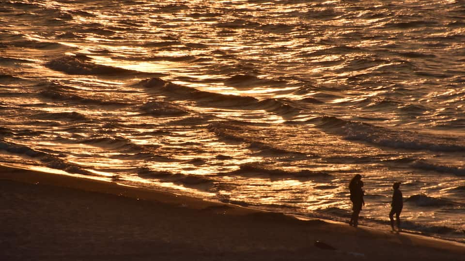 A beach with waves and two people standing on the shore.