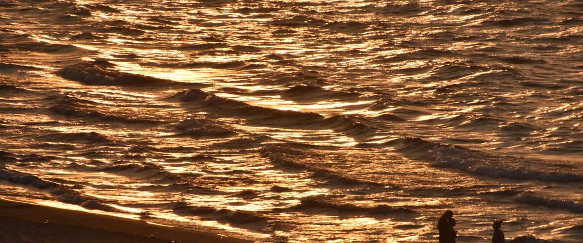 A beach with waves and two people standing on the shore.