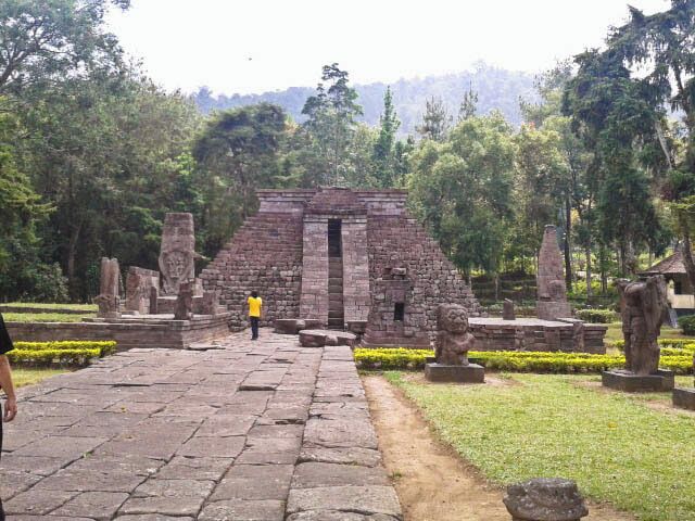 An ancient stone structure with a central doorway, surrounded by statues and a well-maintained garden.