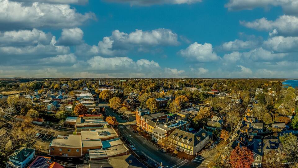 An aerial view of a town with a river, buildings, and surrounding greenery.