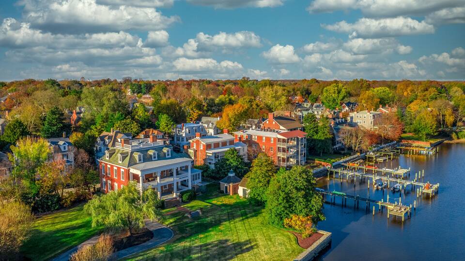 A riverside town with red brick buildings, a dock, and autumn foliage.