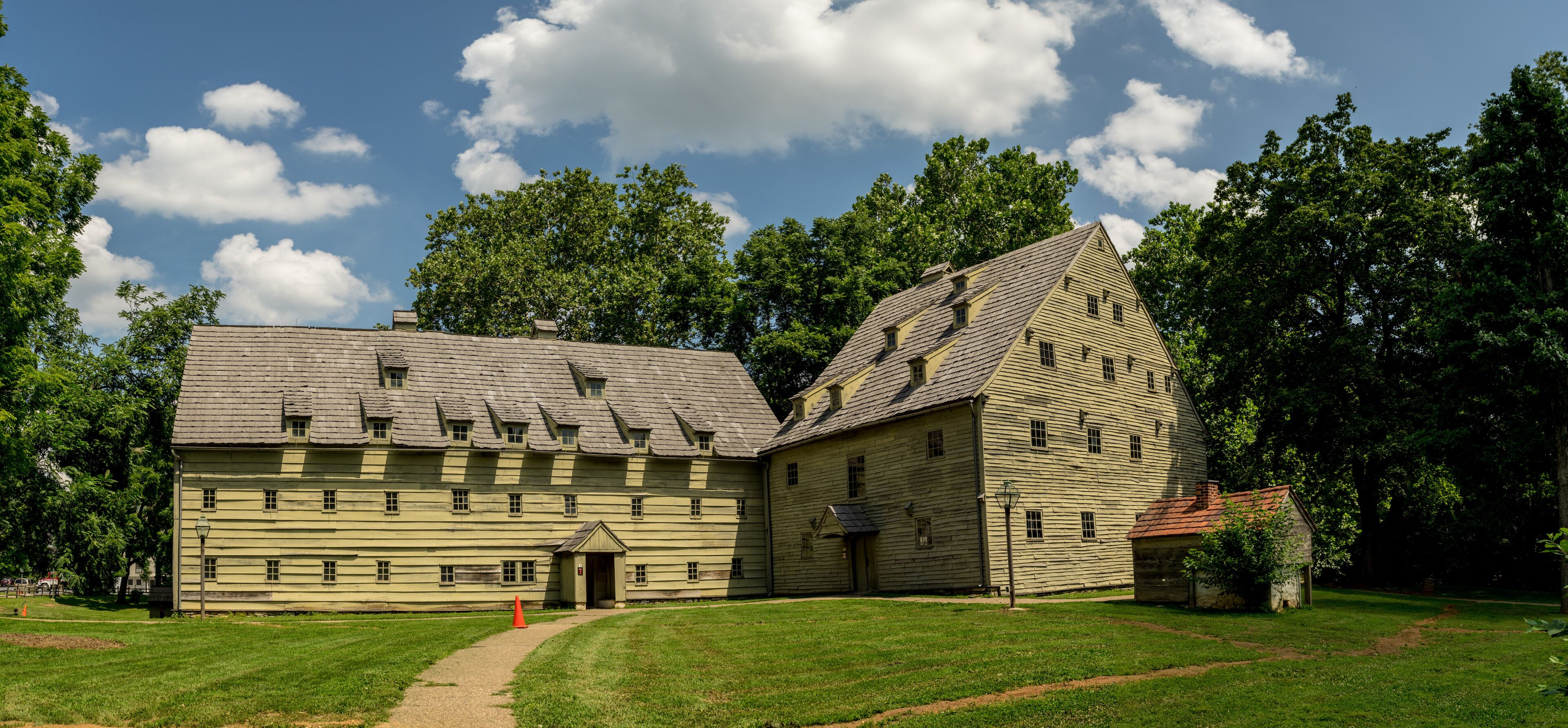 A historic wooden building with a steeply pitched roof, surrounded by lush green trees and a clear blue sky.