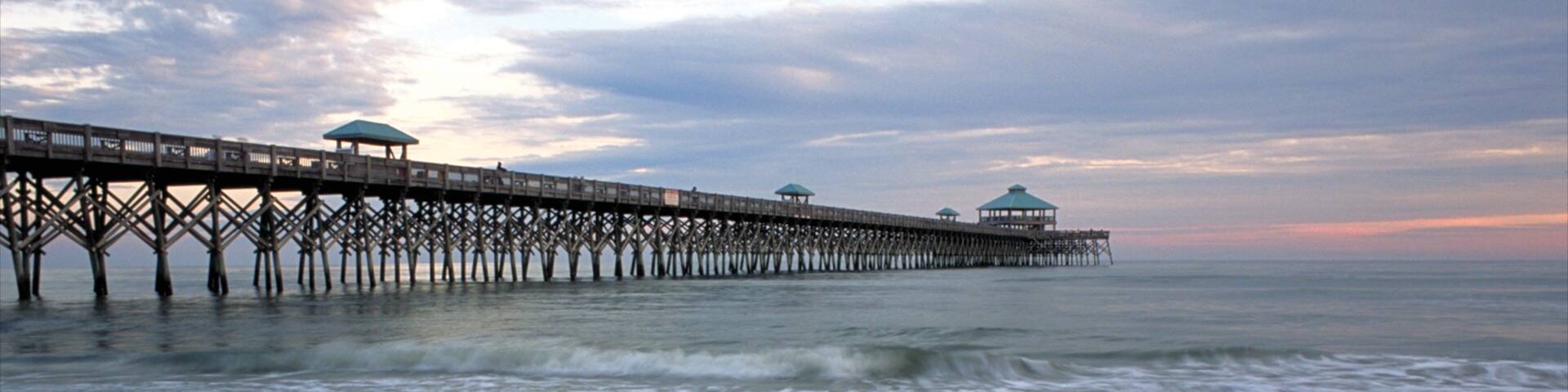 Folly Beach que inclui um pôr do sol, uma ponte e uma praia
