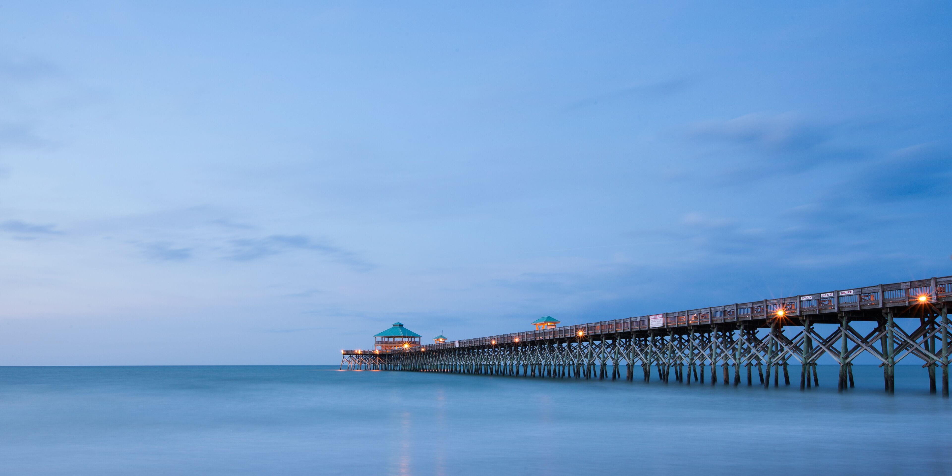 A long pier extending into calm waters at dusk.