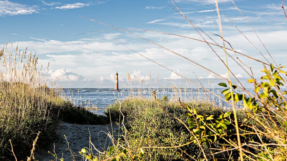 A lighthouse, sandy beach, and seaweed in the foreground.
