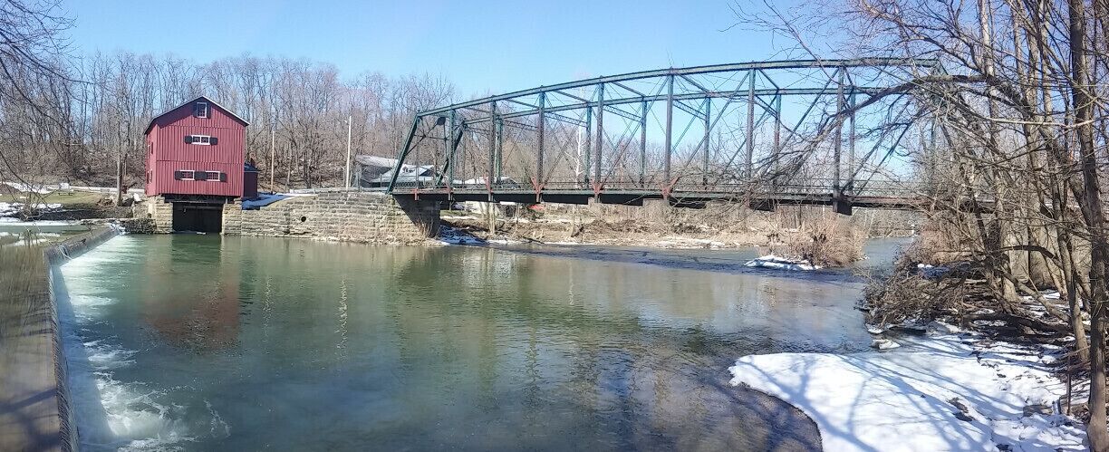 A view of the dam and mill from across the river. This view also includes the Indian Mill bridge, a Pin-connected, 10-panel Pratt through truss bridge built in 1913.