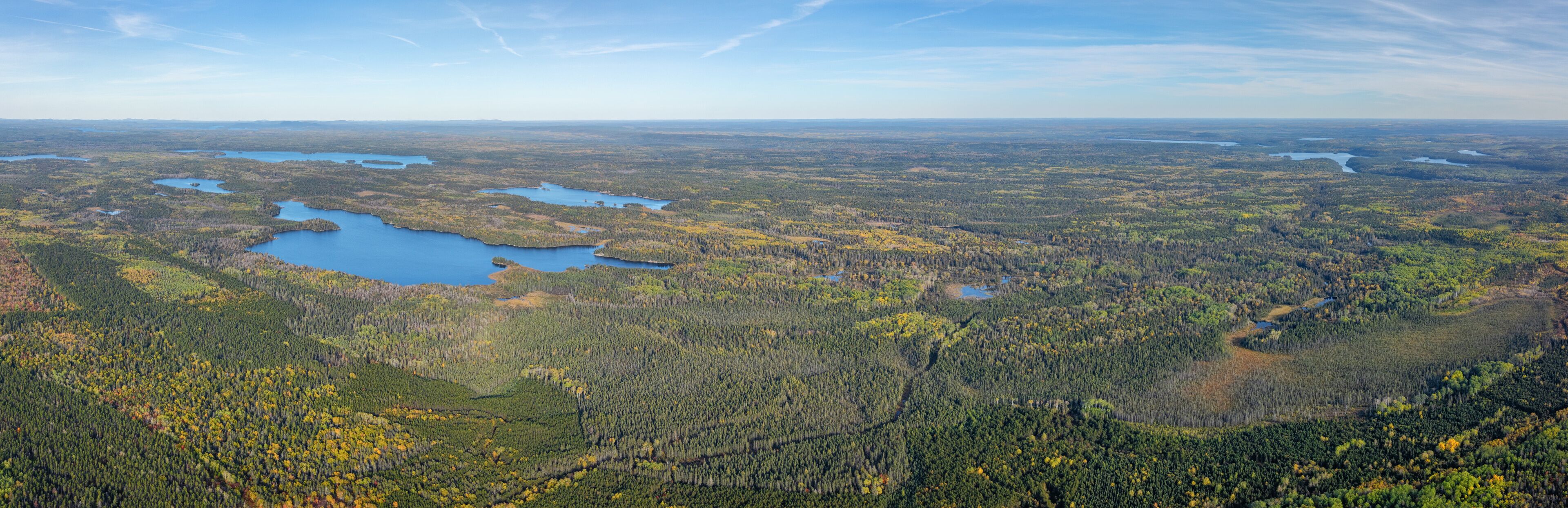 A vast forested landscape with multiple lakes and a clear sky.