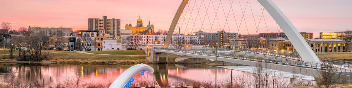 A park with a large white arch bridge, a domed building, and a calm lake reflecting the sunset.