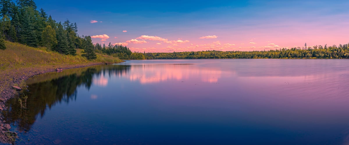A calm lake with a forested shoreline and a clear sky.