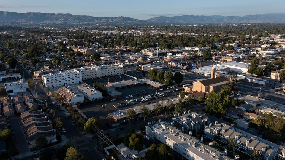 An aerial view of a city with a large industrial area, residential buildings, and a mountainous backdrop.