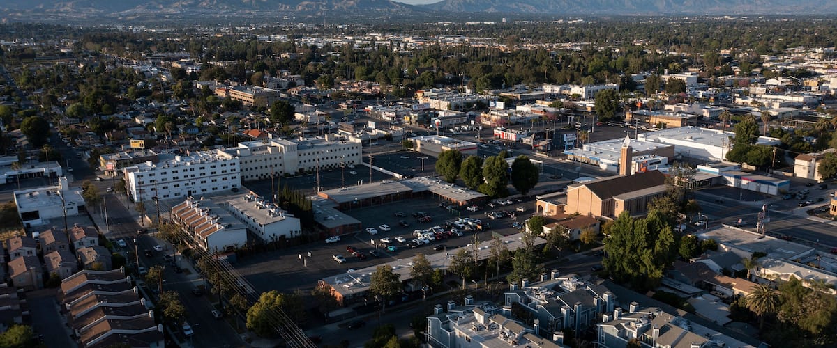 An aerial view of a city with a large industrial area, residential buildings, and a mountainous backdrop.