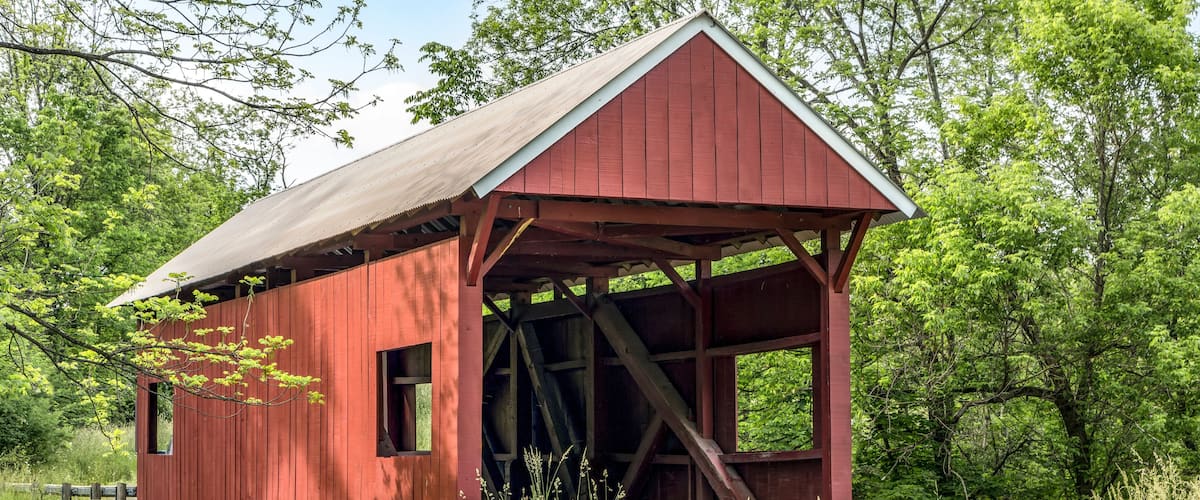 The historic red Erskine Covered Bridge crosses Middle Wheeling Creek in rural wooded Washington County, Pennsylvania.