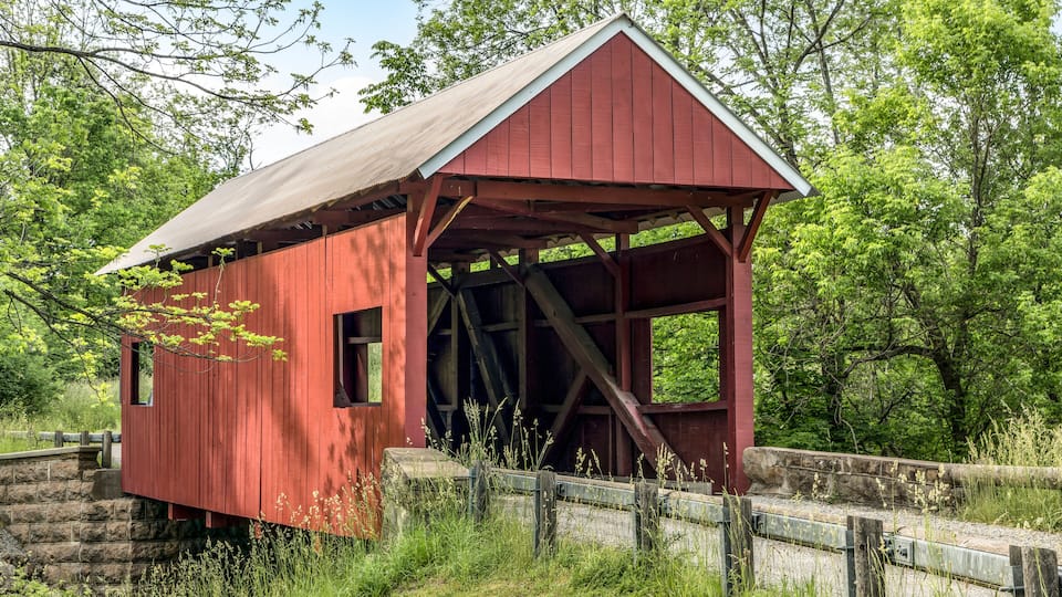 A red covered bridge in a wooded area.