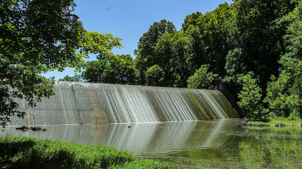 A dam with water cascading down, surrounded by lush greenery and trees.