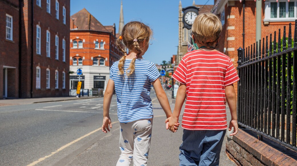 Two kids hold hands, walk down sunny street together Farnham, UK