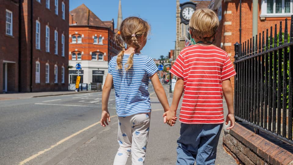 Two children walking on a street with historic buildings and a clock tower in the background.