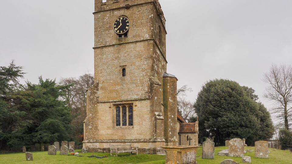 A historic tower with a clock, surrounded by a cemetery with headstones.