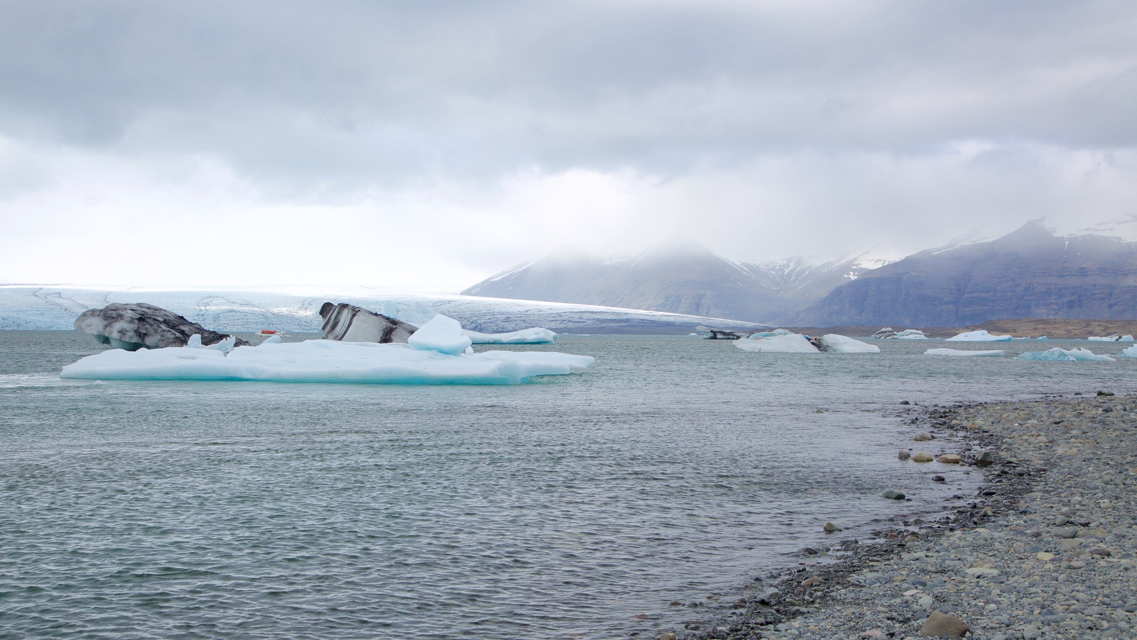 A glacier with floating icebergs in a fjord, surrounded by mountains.