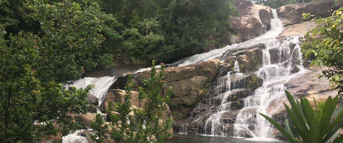 A multi-tiered waterfall surrounded by dense greenery and rocks.