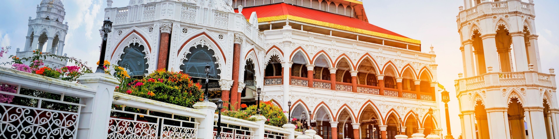 A grand architectural structure with ornate white and red detailing, a prominent golden dome, and statues on top.