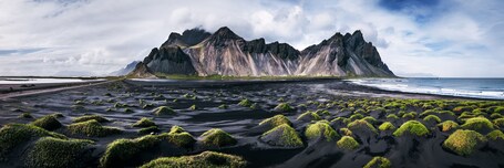 Eine Küstenlandschaft mit einer markanten Bergkette und grün bewachsenen Felsen.