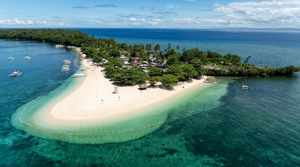Vista aérea de una isla tropical con una playa de arena blanca, aguas turquesas cristalinas y algunas embarcaciones dispersas.