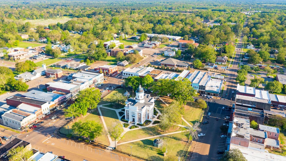 An aerial view of a town with a prominent church, wide streets, and surrounding greenery.