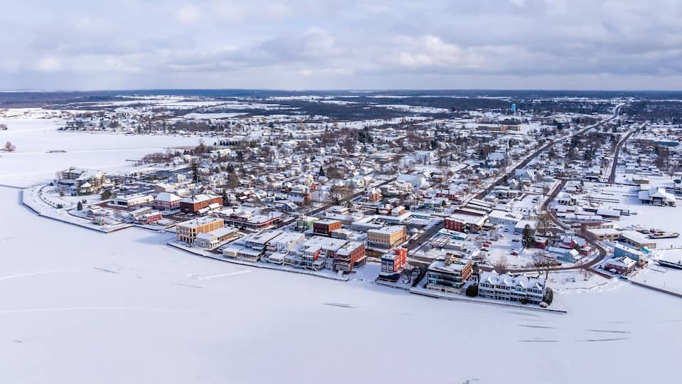 A snow-covered town with a mix of residential and commercial buildings, a prominent church, and a large water tower in the distance.