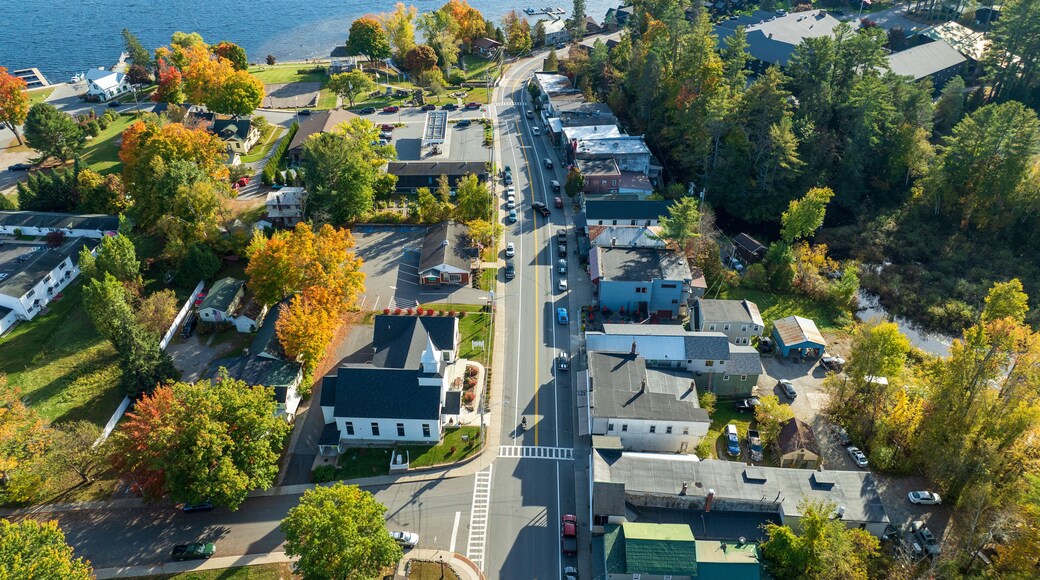 Aerial view of Schroon Lake, New York, showcasing the calm lake, fall foliage, and small town structures nestled along the shoreline under a clear sky.