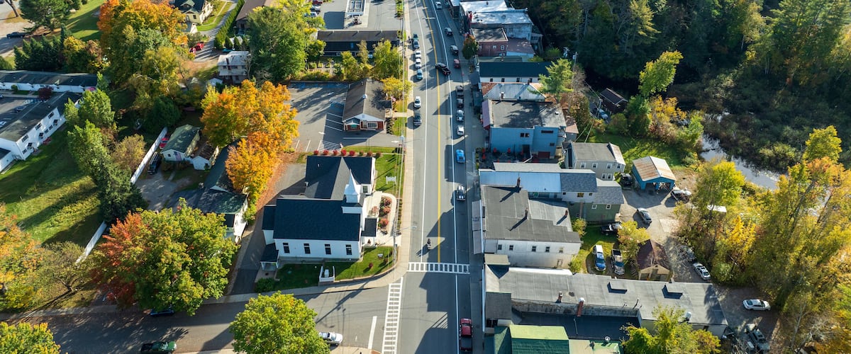 Aerial view of Schroon Lake, New York, showcasing the calm lake, fall foliage, and small town structures nestled along the shoreline under a clear sky.