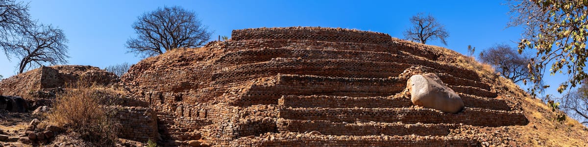 Ancient brick ruins with a large stone slab on top, surrounded by dry, rocky terrain and sparse vegetation.