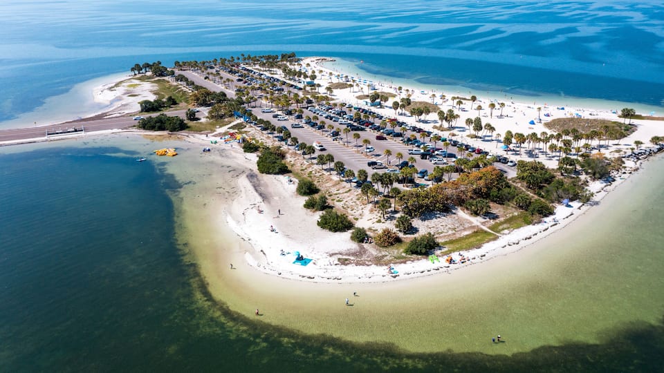 An aerial view of a coastal resort with a beach, parking area, and clear blue waters.