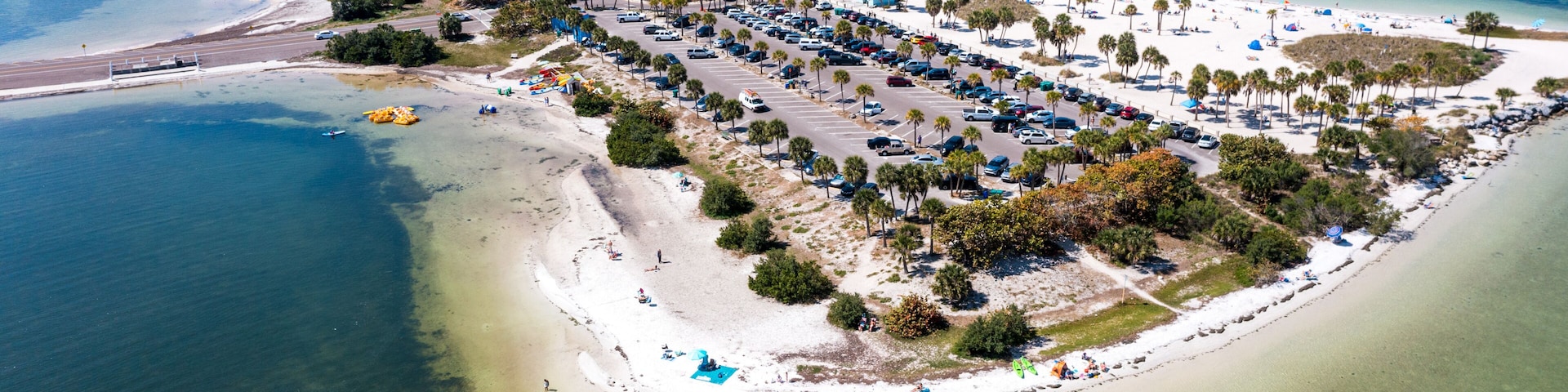 Luftaufnahme eines Küstenresorts mit Strand, Parkplatz und blauem, klarem Wasser.