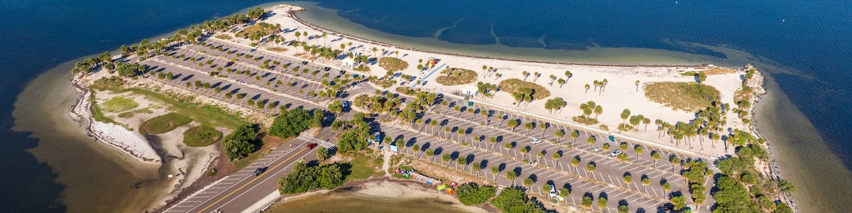 Aerial view of Fred Howard Park in Tarpon Springs, Florida, featuring parking lots, palm trees, sandy beaches, and surrounding blue waters under a clear sky.