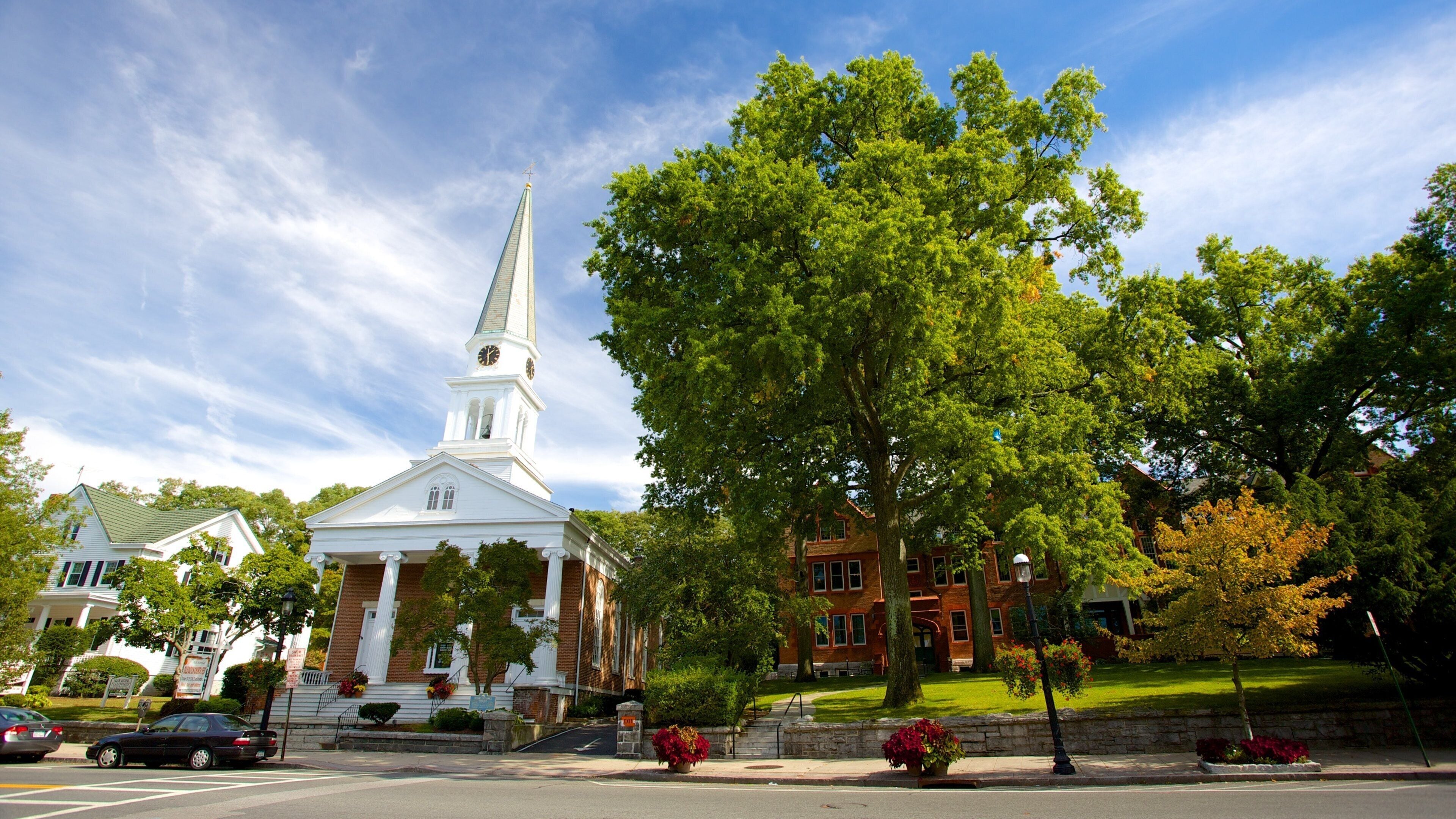 A church with a steeple, surrounded by trees and a brick building.