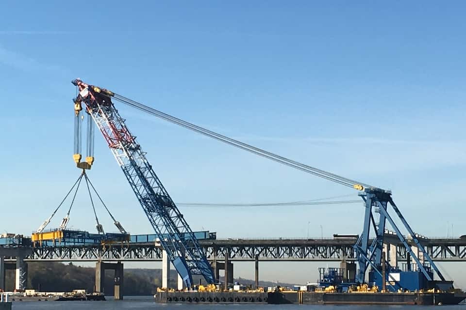 A large blue crane lifting a load over a bridge.