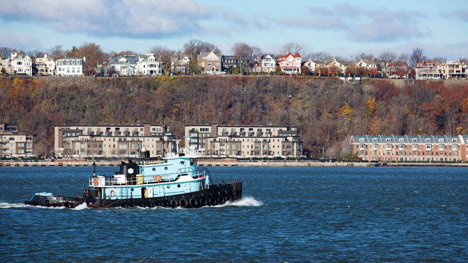 A river with a blue boat, houses along the riverbank, and autumn-colored trees.