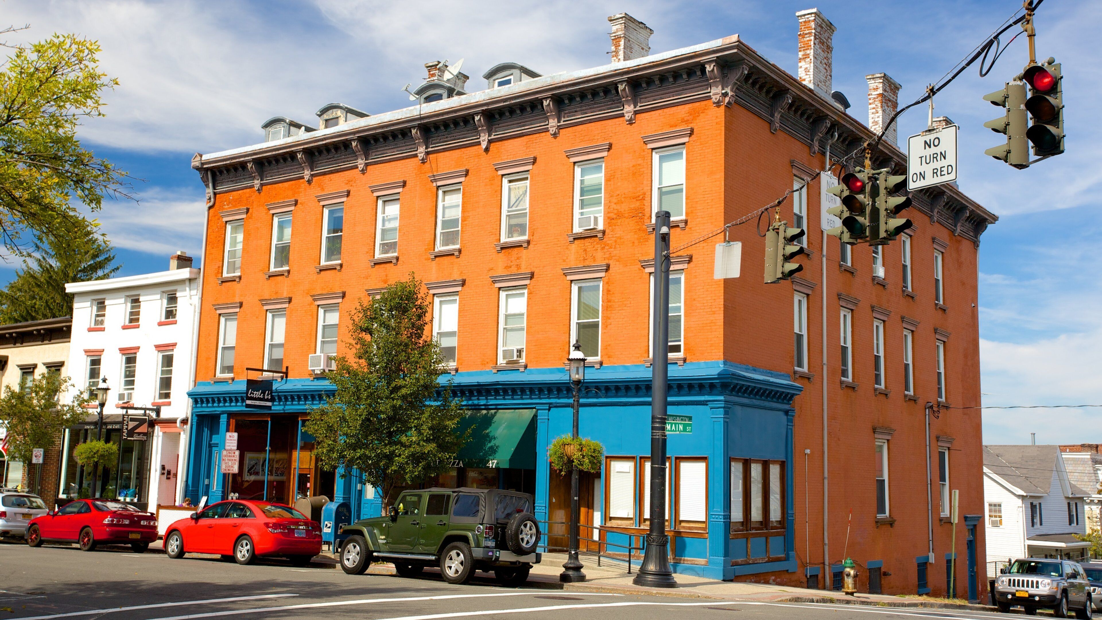 A red brick building with blue trim, a green SUV, and a red car parked in front.
