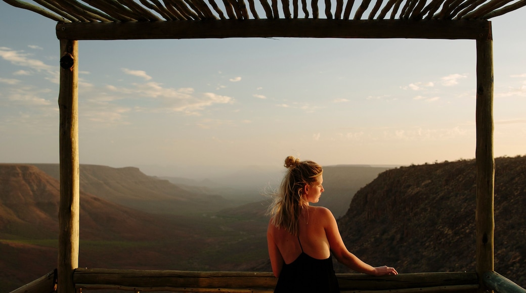 A person in a black dress standing on a wooden deck with a view of a mountainous landscape.