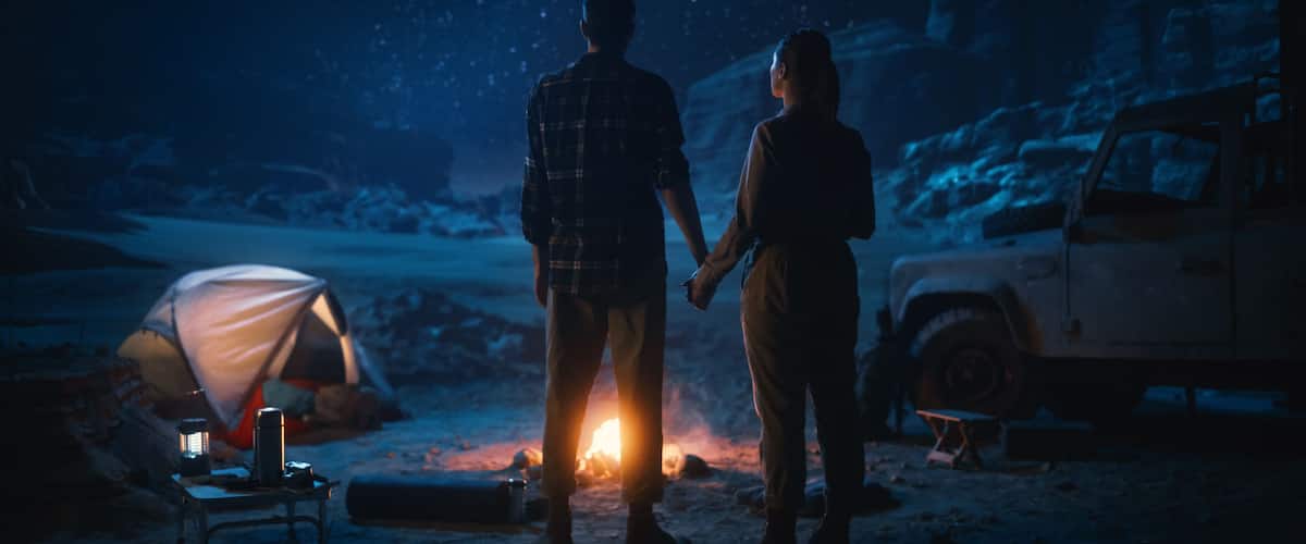 Happy Couple Camping in the Canyon at Night, Standing by Campfire, Holding Hands Lovingly and Romantically Watching Star Sky. Two Traveling people on a Nature Inspirational Vacation Trip, Journey
