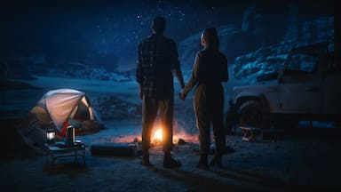 Happy Couple Camping in the Canyon at Night, Standing by Campfire, Holding Hands Lovingly and Romantically Watching Star Sky. Two Traveling people on a Nature Inspirational Vacation Trip, Journey