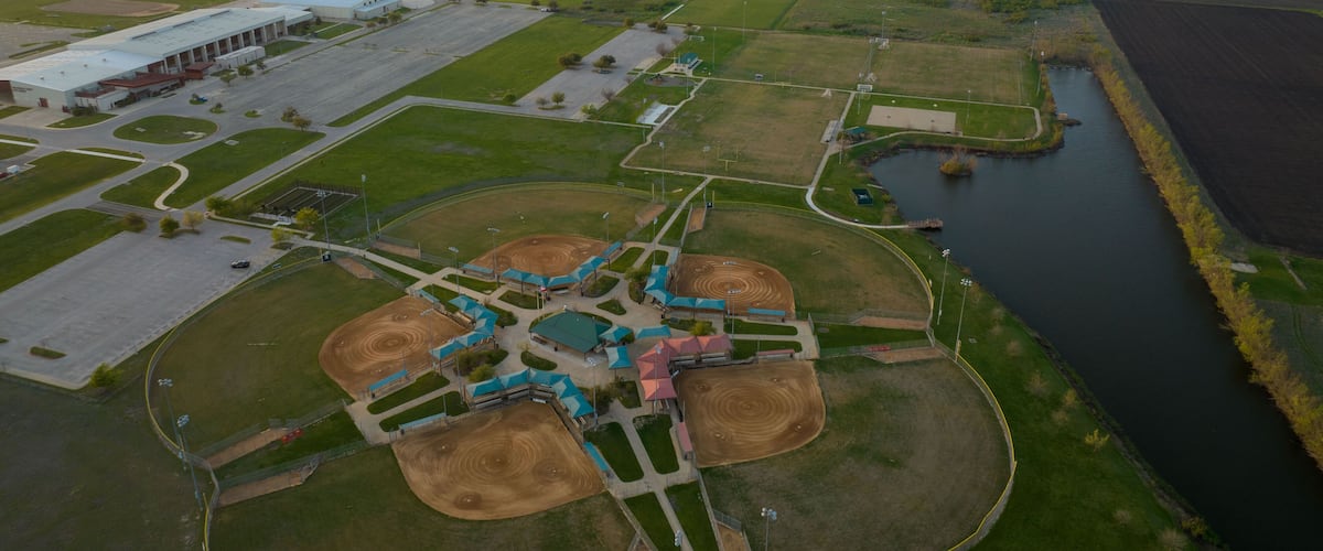 An aerial view of a baseball field with a stadium, a river, and surrounding fields.