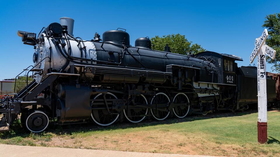 A large black steam locomotive with the number 401, parked on a grassy area near a railroad crossing sign.