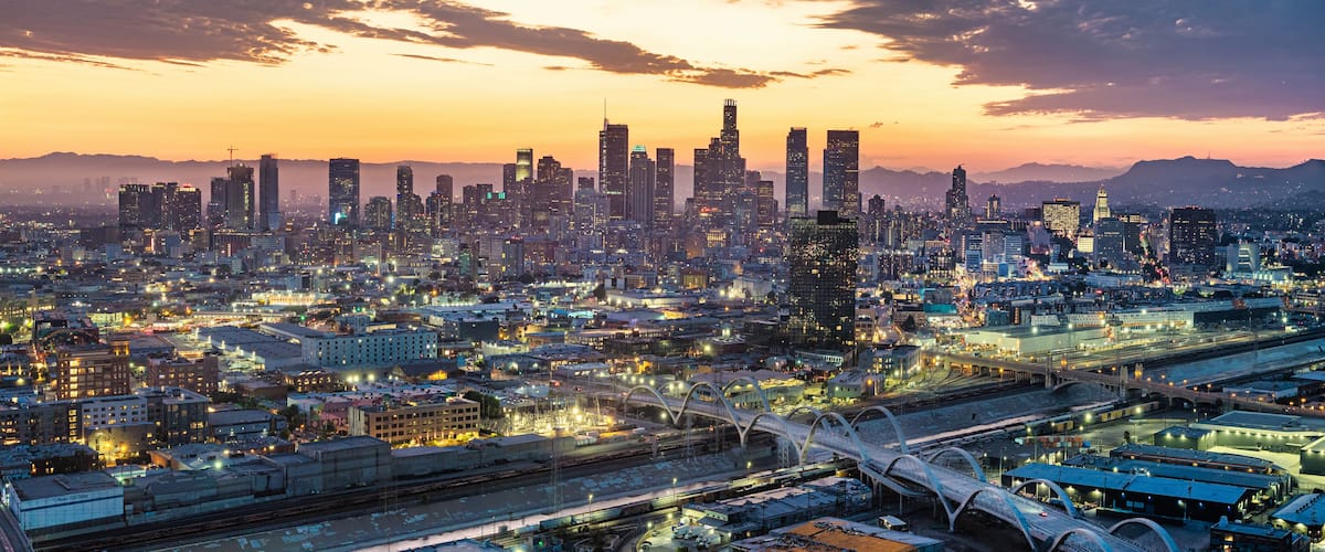 Un horizonte urbano al atardecer con edificios iluminados y un puente.