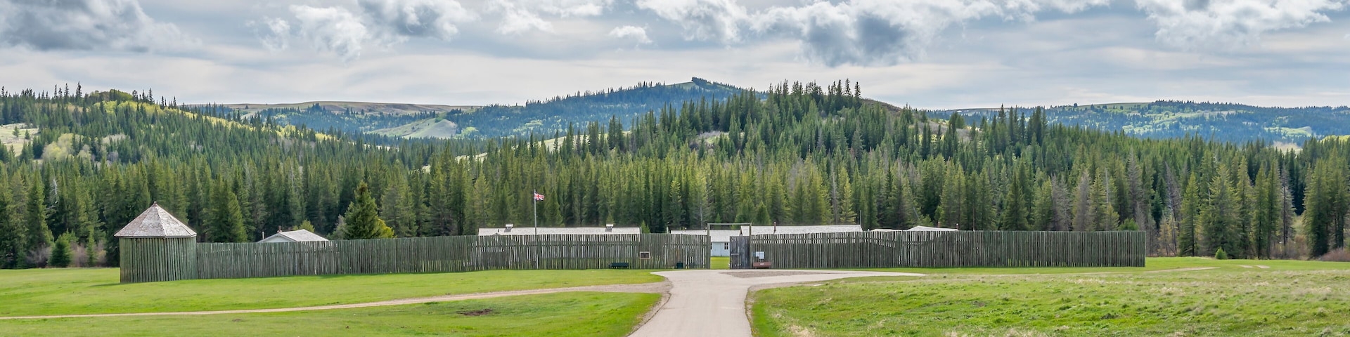 A rural road leading to a wooden fence and buildings, surrounded by dense forests and hills.
