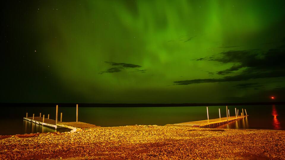 A pier extending into a calm body of water under a vibrant green aurora.