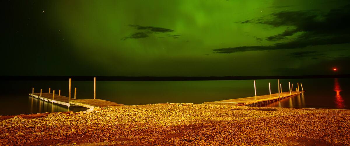 A pier extending into a calm body of water under a vibrant green aurora.