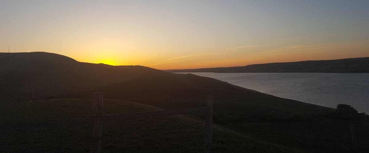 A sunset over a lake with hills in the foreground and a clear sky.
